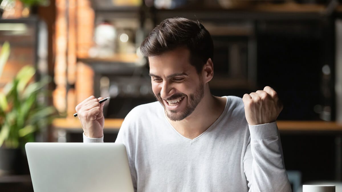 a man sitting at his computer smiling with his fists in the air