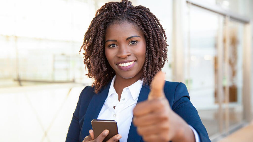 a woman in a blue suit holding her cell phone and giving a thumb's up