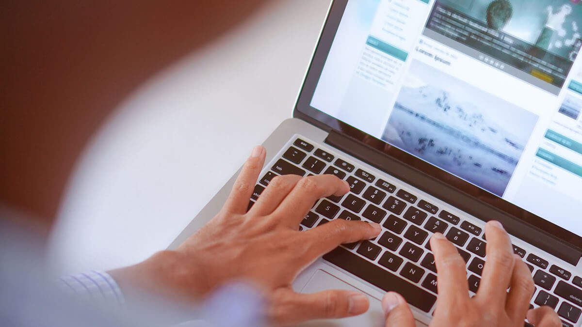 a persont typing on a laptop with articles on the screen